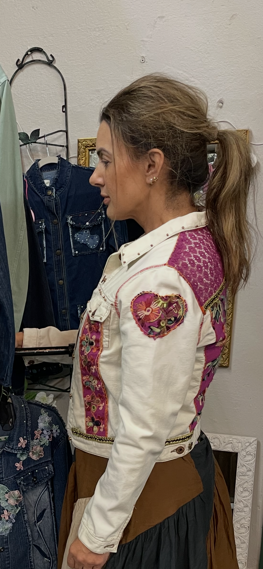 Back view of custom ivory denim jacket with magenta embroidery panel next to denim jacket rack